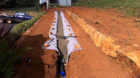 Drainage trench with gravel and slotted pipe alongside a new sandstone retaining wall