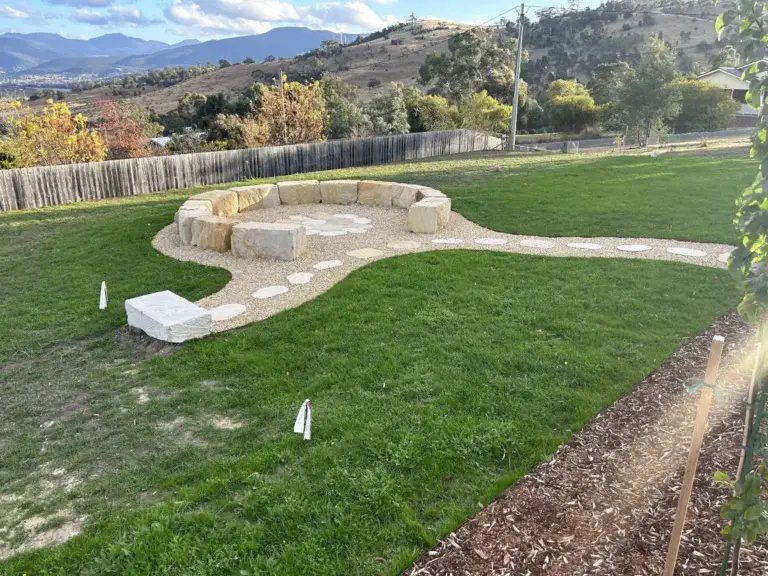 Sandstone boulder fire pit circle with a curving gravel path across the lawn, Honeywood