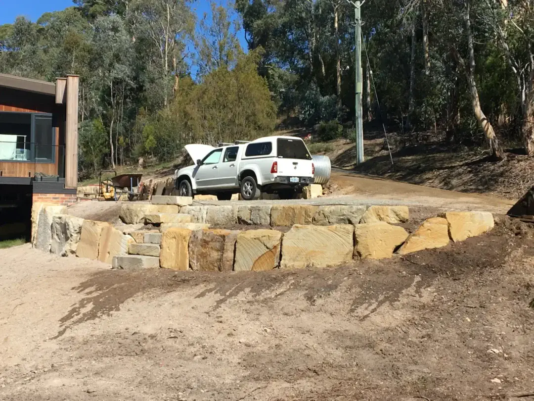 Curved sandstone boulder retaining wall forming a level parking area beside the house