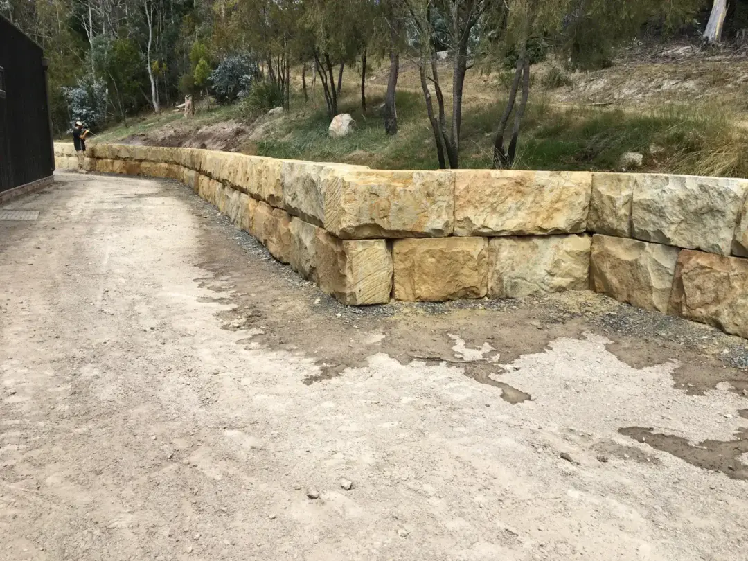 Two-course sandstone boulder retaining wall running alongside the new driveway