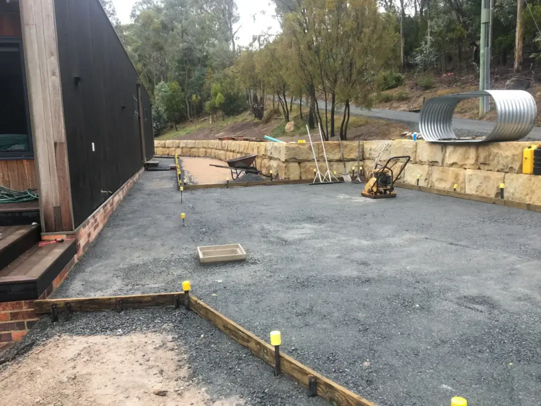 Compacted gravel base being prepared for a new outdoor area beside the sandstone retaining wall