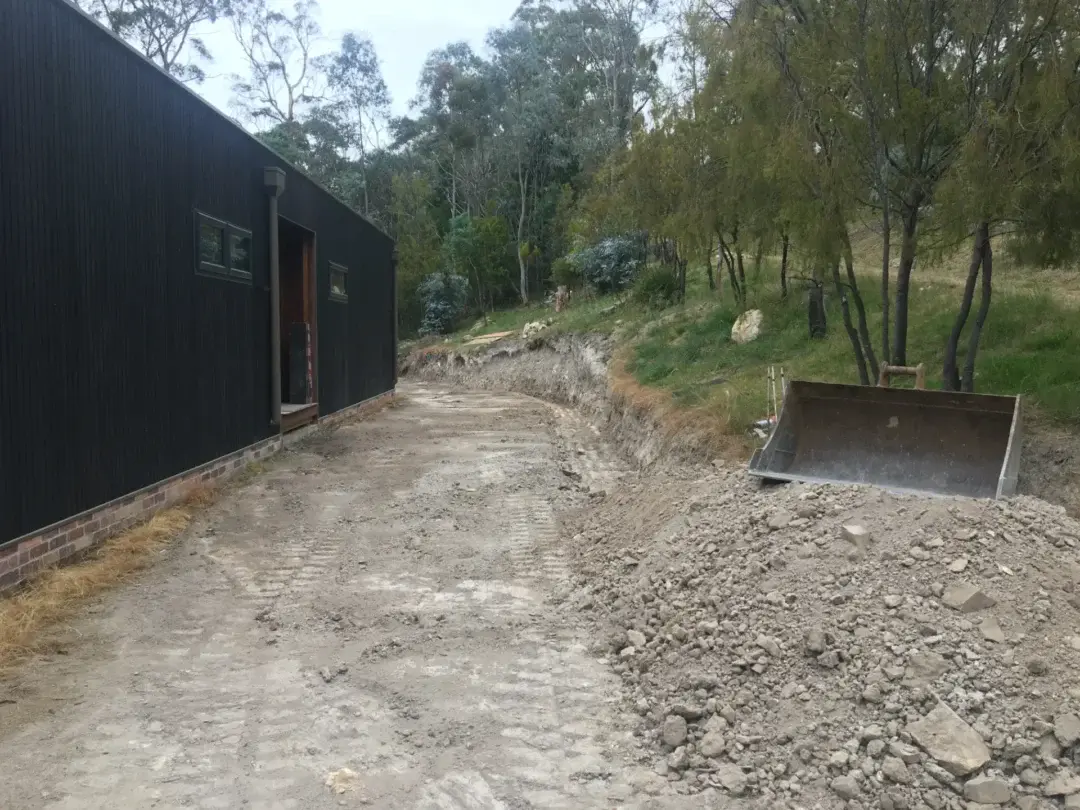 Excavator cutting a new driveway alignment beside the house