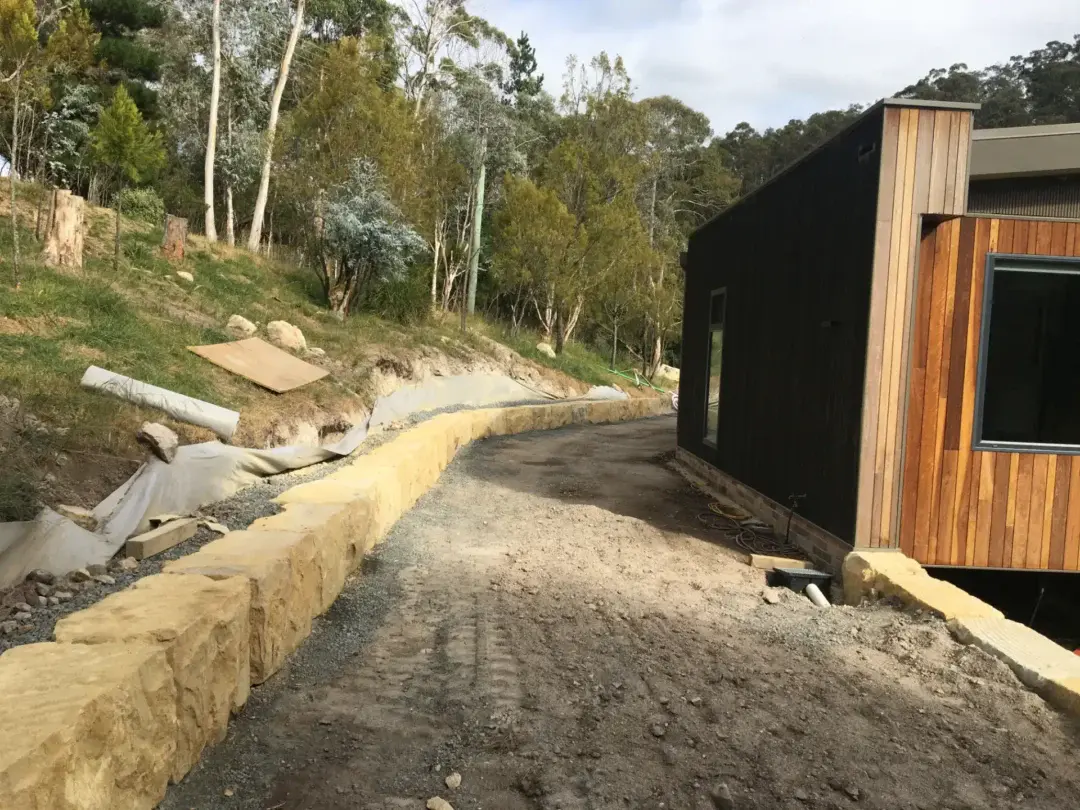 Finished sandstone boulder retaining wall curving along the driveway beside the house