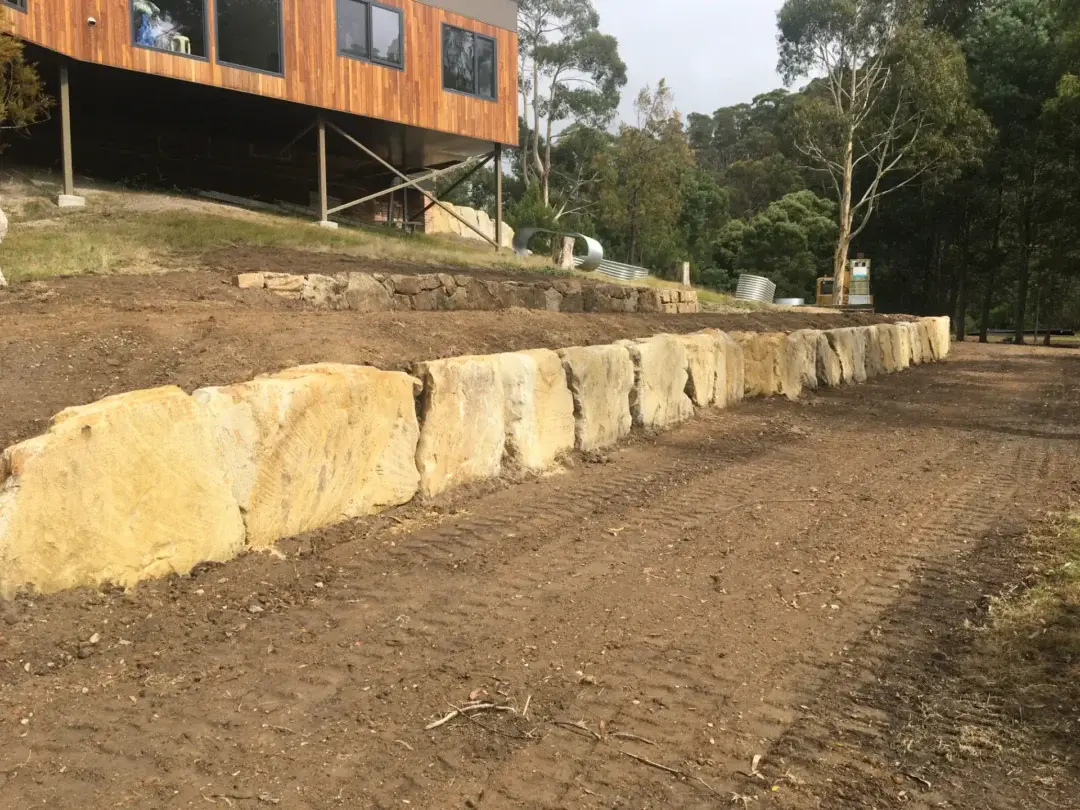Sandstone boulder retaining wall built below a timber-clad home on a steep block