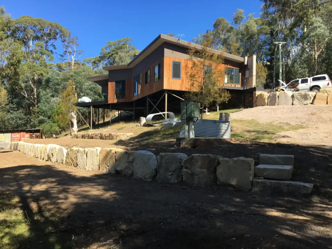 Modern home on stilts on a steep Kingston block, with a new sandstone boulder retaining wall and steps in the foreground