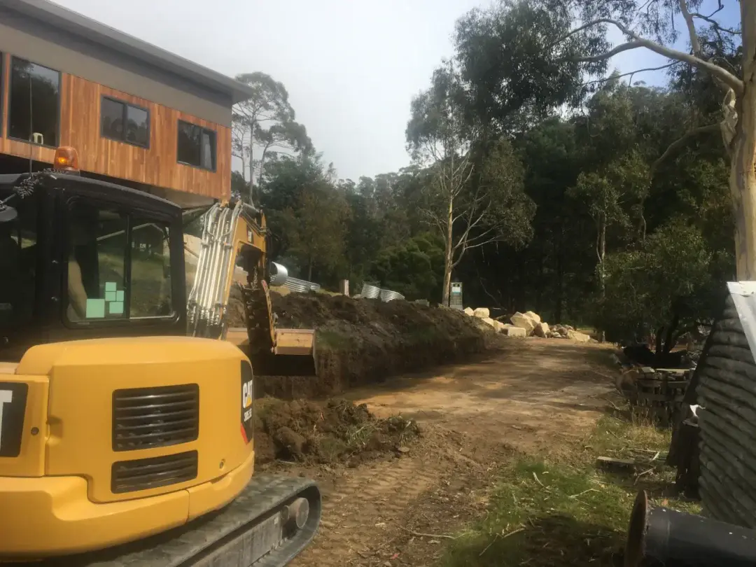 Excavator grading the site beside the house before retaining wall works