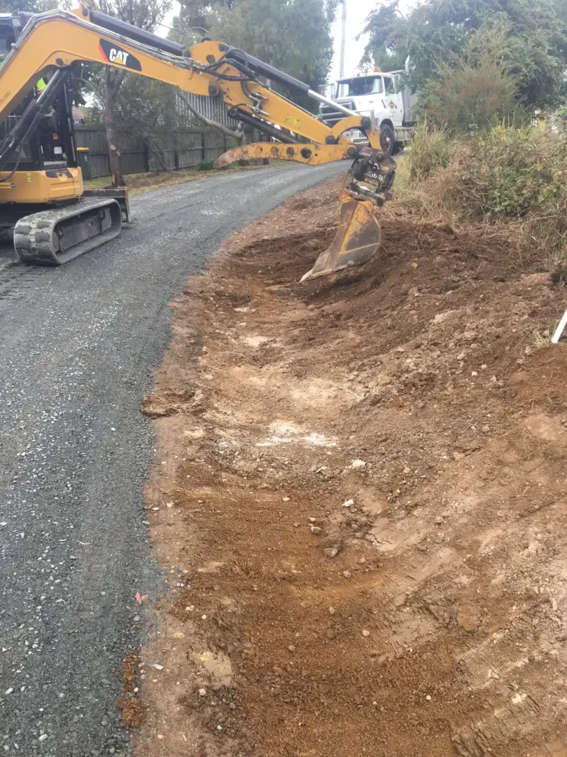 Excavator trenching alongside the driveway, carefully working around underground services