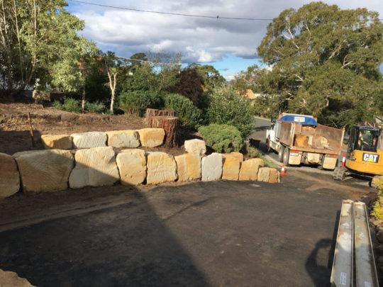 Widened driveway with a new sandstone boulder retaining wall, excavator and truck on site