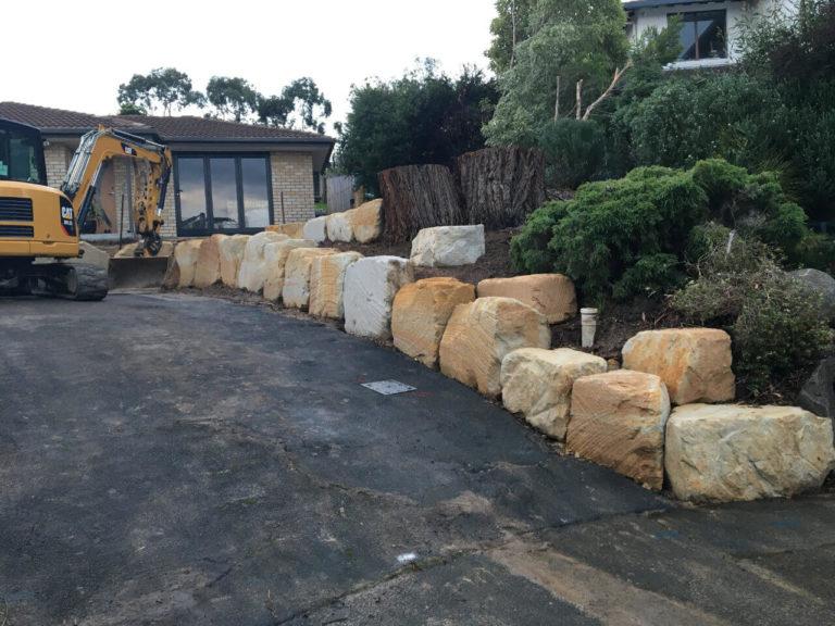 Two-tier sandstone boulder retaining wall along a widened driveway in Lindisfarne