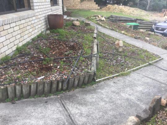 Old timber log garden edging and exposed irrigation lines before replacement