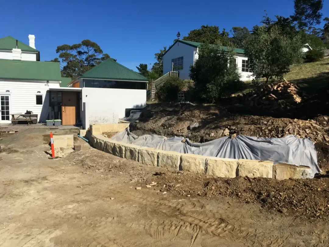 Sandstone block wall curving between two houses, with drainage fabric laid behind it