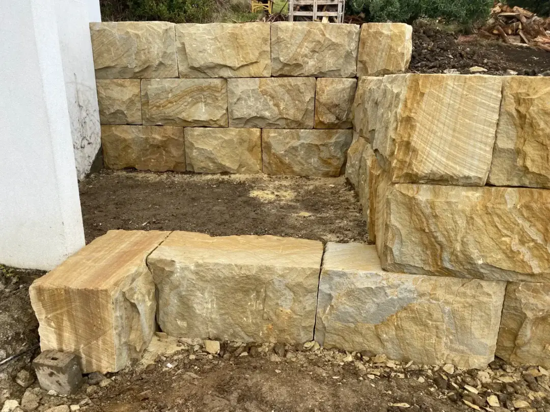Close-up of a finished sandstone block retaining wall corner forming a garden bed against the house
