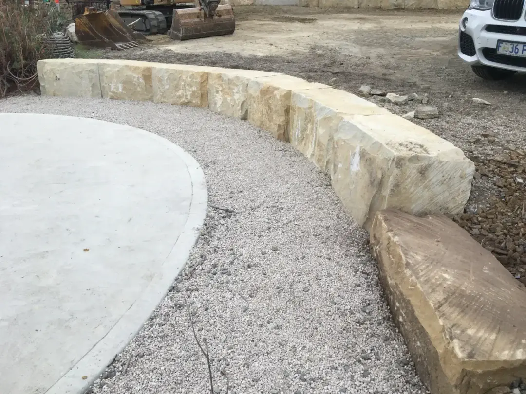 Curved sandstone boulder wall around a new gravel and concrete parking area