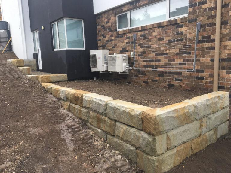 Sandstone boulder retaining wall along the side of a house in Tranmere